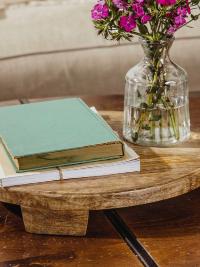 Closeup of large wood tray with books and flower vase atop while placed on a coffee table. 