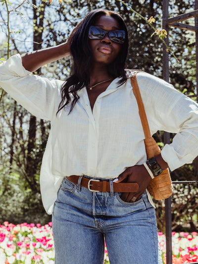Woman in a white blouse and jeans wearing oversized black sunglasses, accessorized with a tan shoulder bag and statement bracelets.