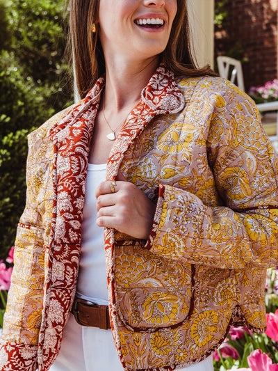 Close-up of a woman smiling and adjusting her red and yellow floral quilted jacket, showing the vibrant block print details and layered look.
