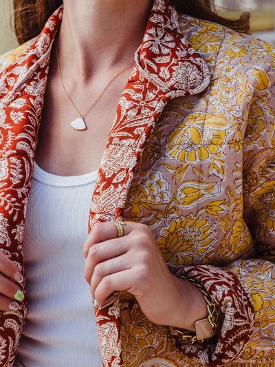 Detail shot of the floral quilted jacket's red inner lining and gold jewelry, featuring a white enamel necklace, gold ring, and bracelet.