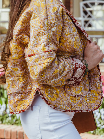Side view of a floral quilted jacket with yellow flowers and red accents, showing the curved hem and printed fabric detail.