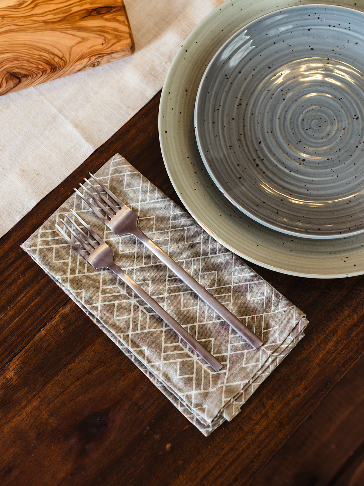 Handcrafted neutral cotton napkin with modern geometric print, styled with a hammered copper napkin ring on a speckled ceramic dinner plate — ethical, fair trade table décor.