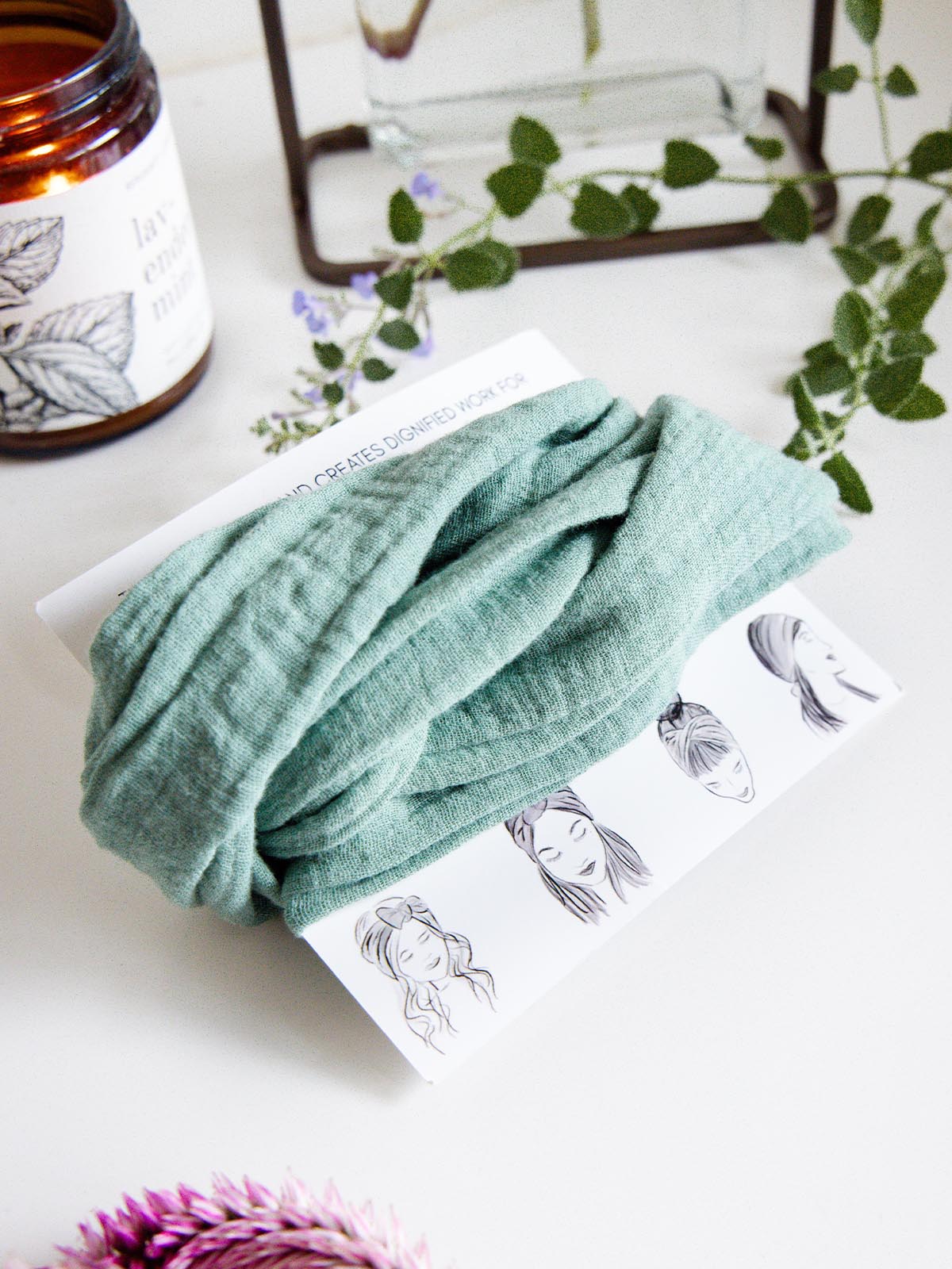 Mint green fabric wrap headband wrapped around a display card, styled with a candle, flowers, and greenery on a white surface.