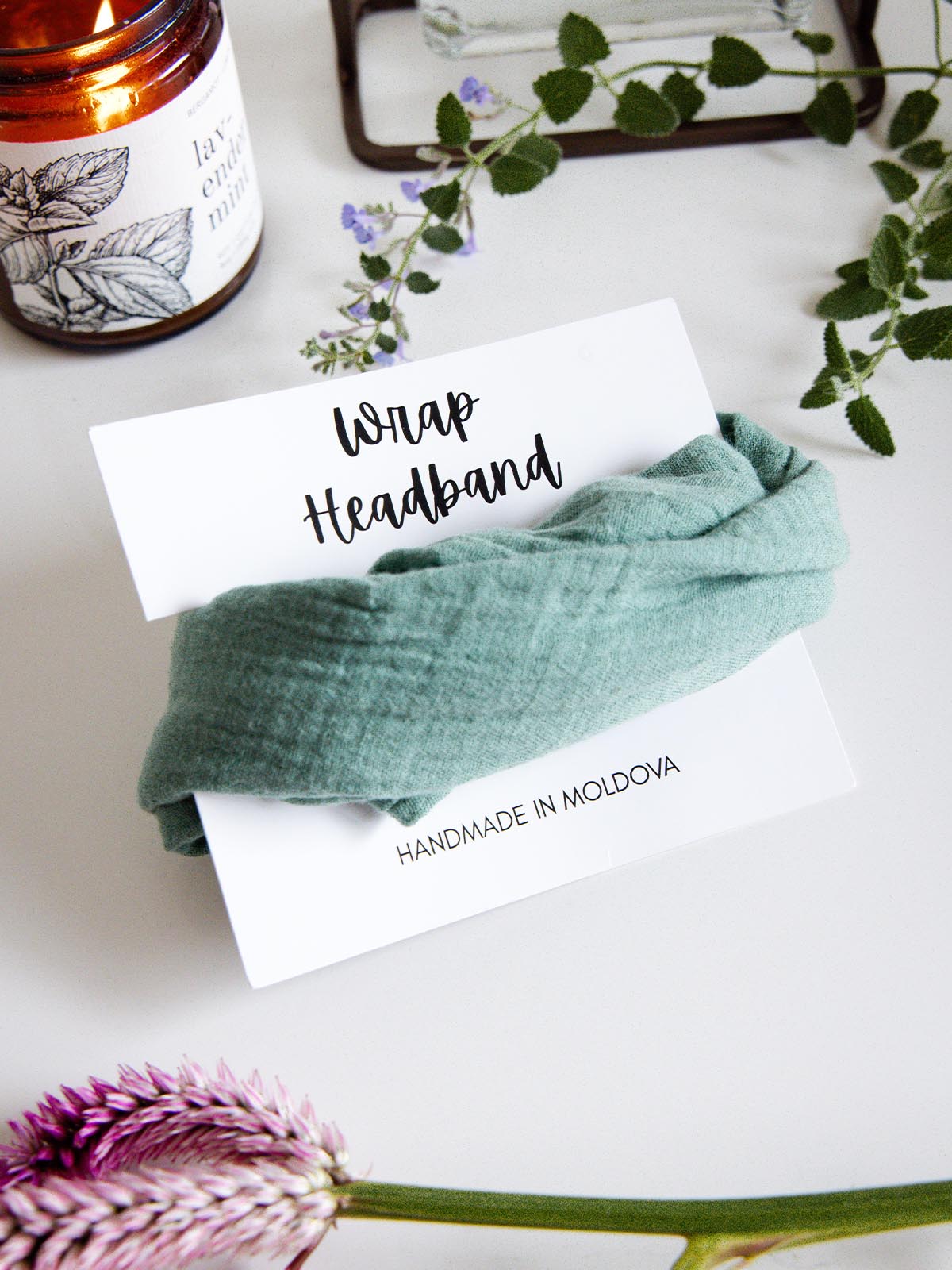Mint green fabric wrap headband labeled 'Handmade in Moldova,' placed on a display card with a lit candle and greenery in the background.