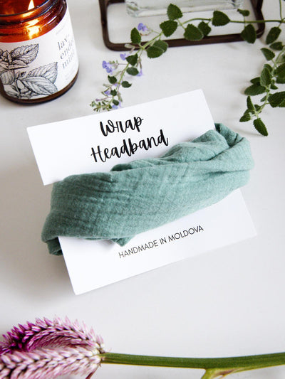 Mint green fabric wrap headband labeled 'Handmade in Moldova,' placed on a display card with a lit candle and greenery in the background.