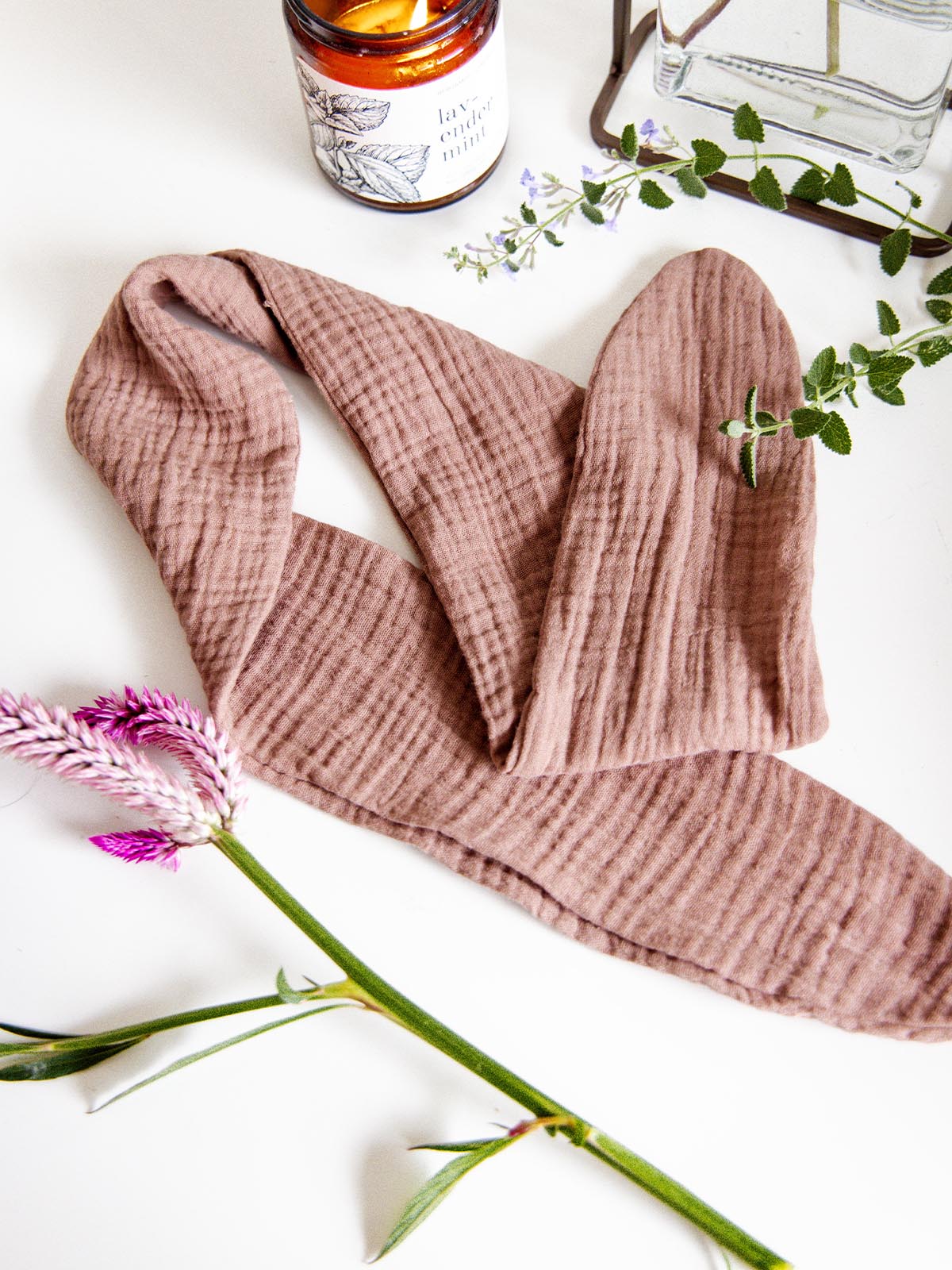 Blush pink fabric wrap headband displayed on a white surface next to a lit candle and flowers, highlighting its soft and textured material.
