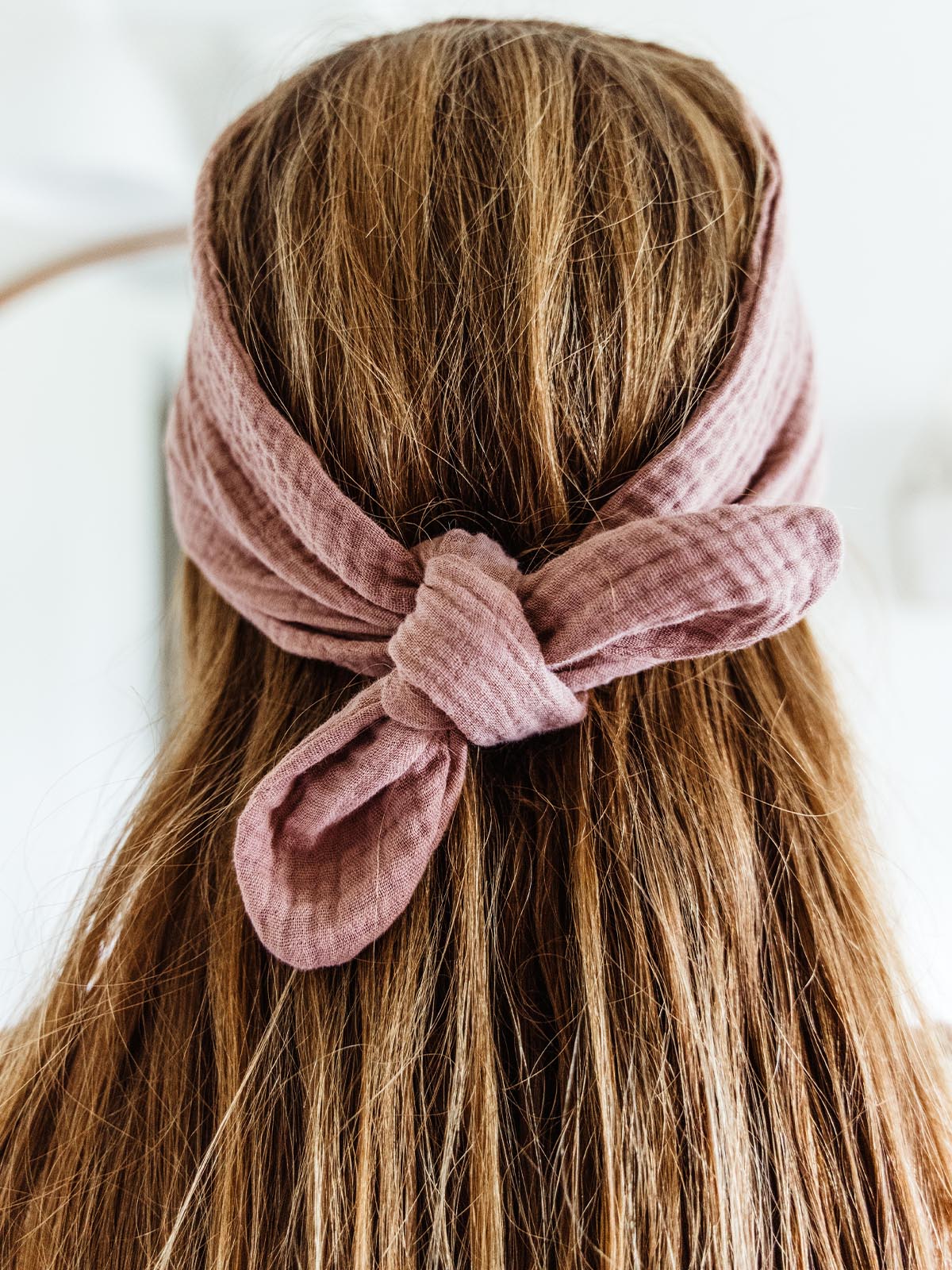 Close-up of a woman’s hair tied with a blush pink fabric wrap headband, emphasizing the soft texture and knotted detail at the back.