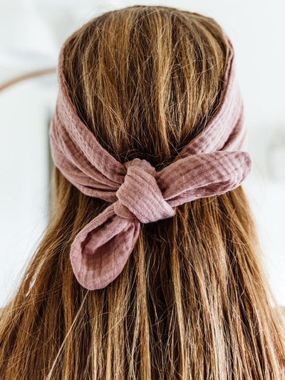 Close-up of a woman’s hair tied with a blush pink fabric wrap headband, emphasizing the soft texture and knotted detail at the back.