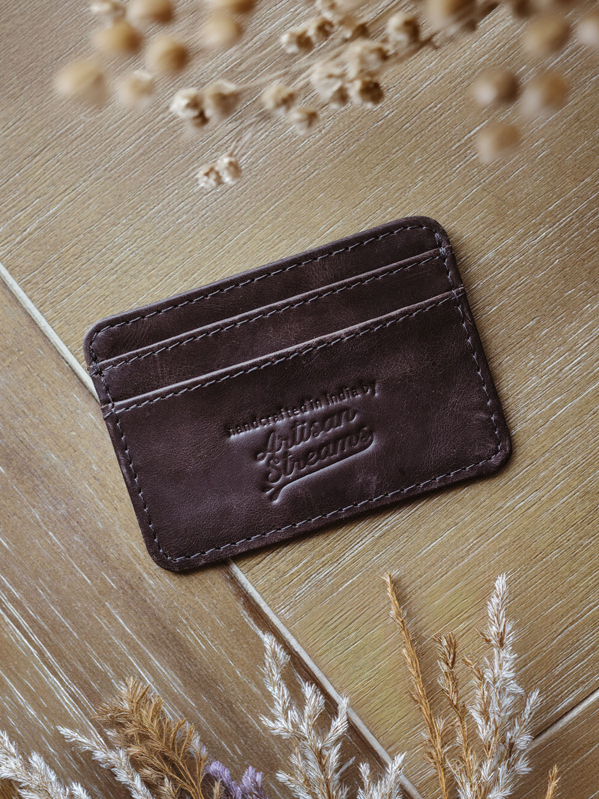 Brown leather card holder with dried flowers on table.