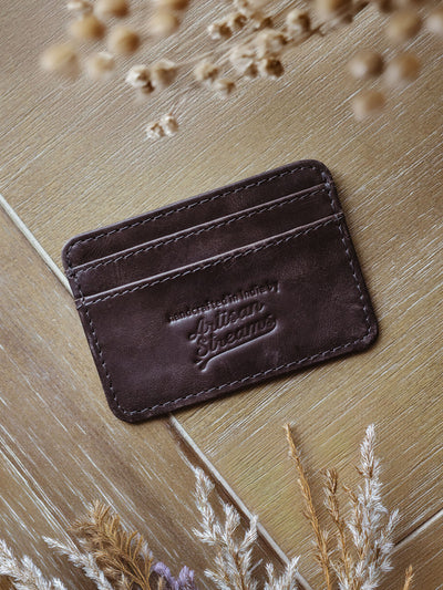 Brown leather card holder with dried flowers on table.