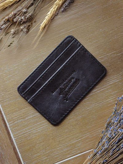 Black  leather card holder with dried flowers on table.