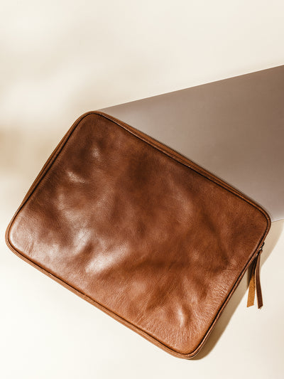 Laptop in brown laptop sleeve on cream background.