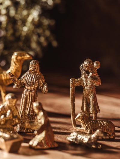 Close-up of a brass nativity figure of a shepherd with sheep, alongside Mary and Joseph.