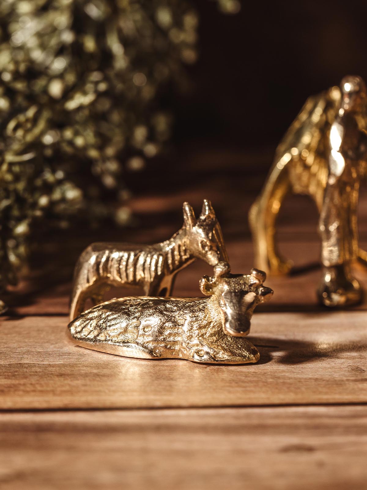 Handcrafted brass figures of a donkey and cow from a nativity scene, placed on a wooden surface.