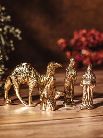 Handcrafted brass nativity figures featuring a camel and three wise men, displayed on a wooden surface with a festive backdrop.