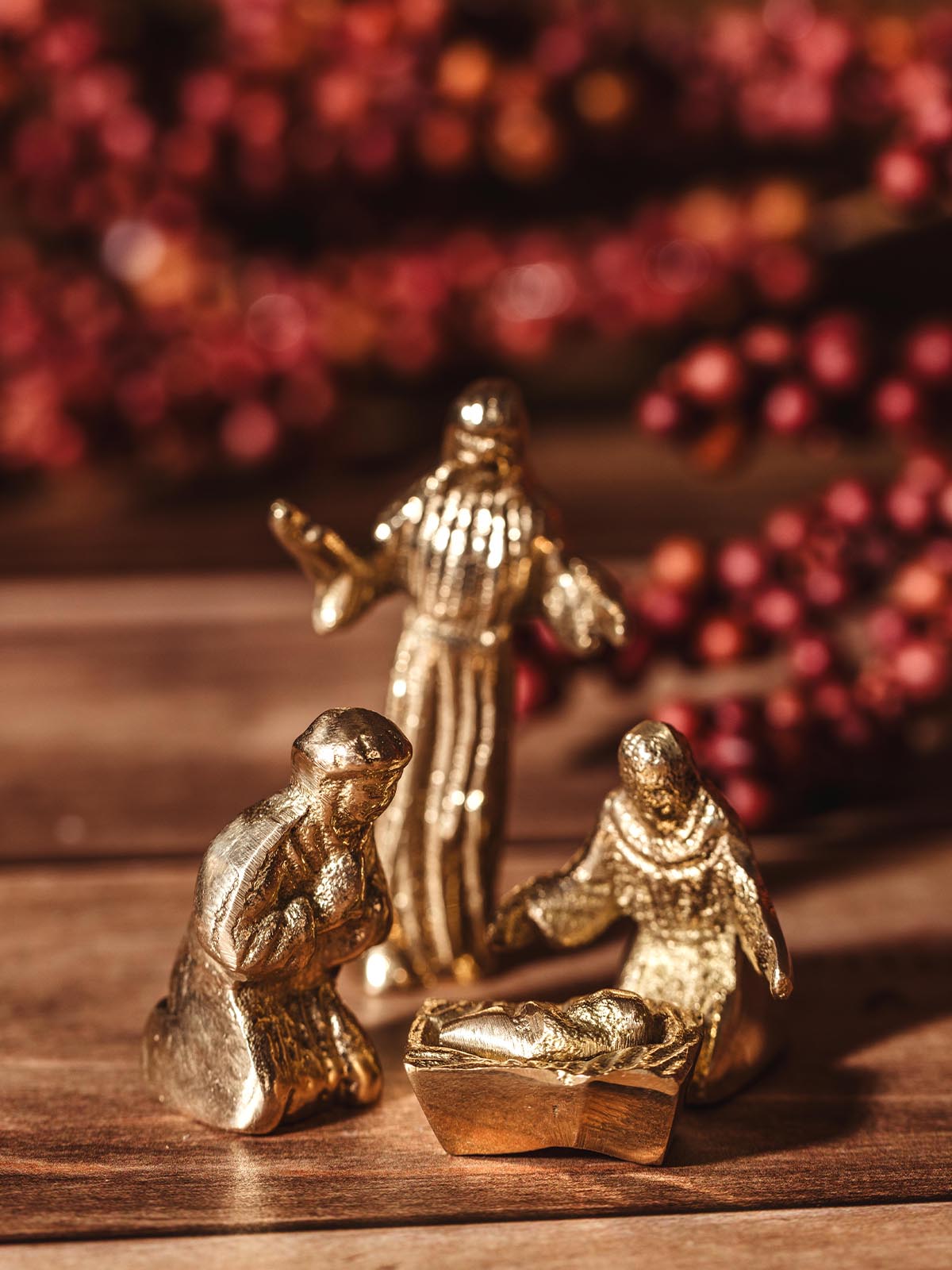 Handcrafted brass nativity figures of baby Jesus in a manger, Mary, Joseph, and a shepherd, set against a festive background.
