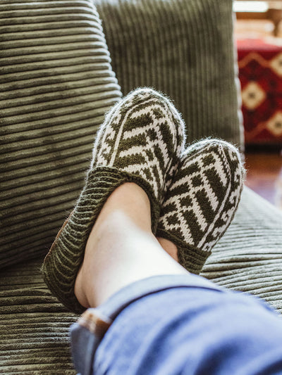 female feet wearing green and white colored handmade slipper socks on a green couch.