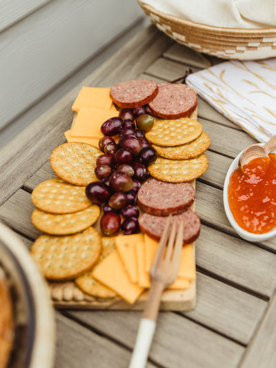 Rectangluar charcuterie board with food atop on outdoor table.