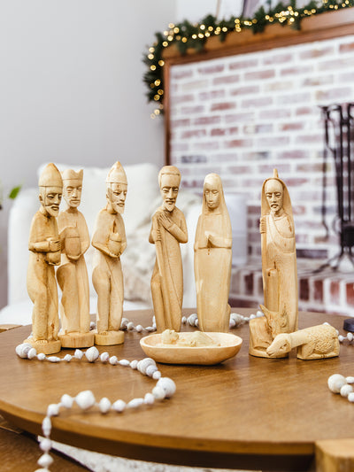 Hand-carved wooden nativity set displayed on a coffee table with beaded garland, featuring Mary, Joseph, baby Jesus, and the three wise men — ethically made holiday décor.
