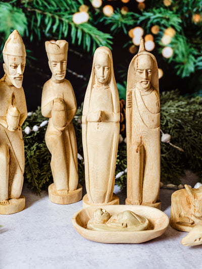 Detailed view of hand-carved wooden Mary, Joseph, and wise men figures with baby Jesus in a wooden manger, styled with natural holiday greenery — sustainable nativity set.