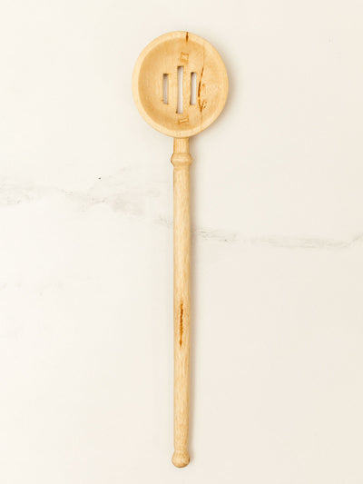 Wooden slotted spoon on white granite counter top.