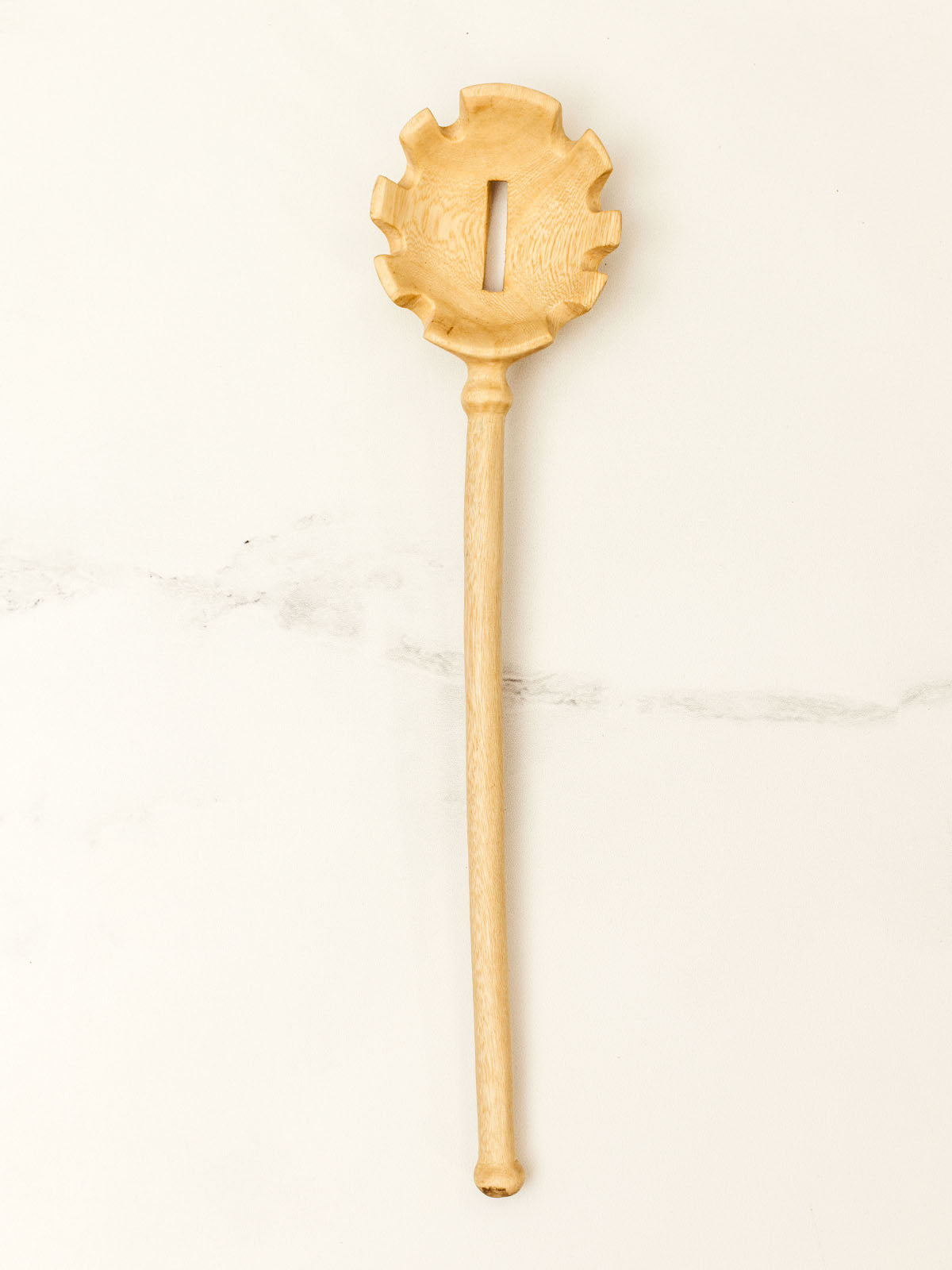 Wooden pasta spoon on white granite counter top.