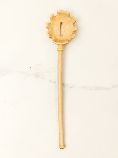 Wooden pasta spoon on white granite counter top.