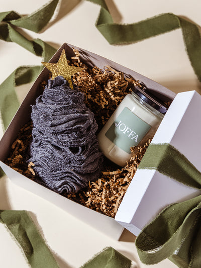 JOFFA candle and charcoal gray washcloth tree nestled in crinkle paper inside a white gift box, styled with olive green ribbon for a festive and professional gifting presentation.