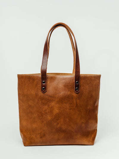 Handmade full-grain leather tote bag with sturdy double handles and brass rivets on a light background. Minimalist everyday carryall ethically crafted for work or travel.