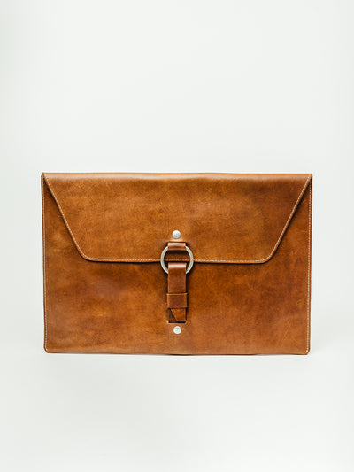 Artisan-made full-grain leather laptop sleeve with flap top, ring-and-strap buckle closure, and clean minimalist design. Sustainable and durable leather accessory.