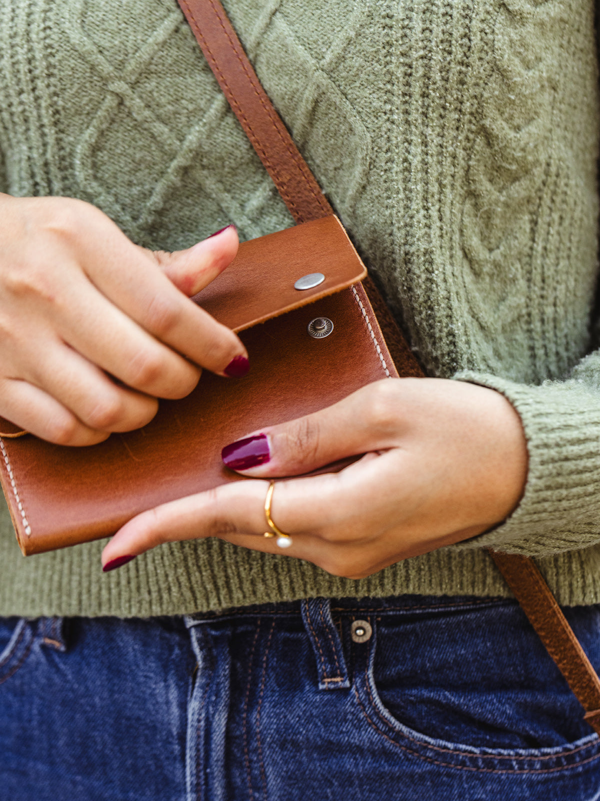 Hands opening a tan leather wallet with silver snap closure, revealing simple card and cash compartments — ethically handcrafted minimalist wallet.