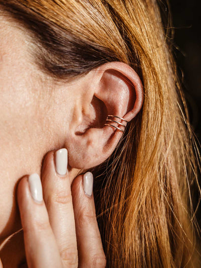Close-up of a woman wearing a minimalist silver ear cuff with three sleek bands, styled with light blonde hair and a natural manicure, showcasing modern artisan-made jewelry.