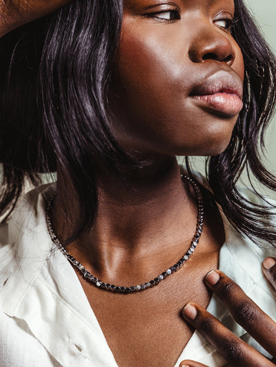 Close-up of a woman wearing a short silver-toned chain necklace with faceted circular links, styled with a white blouse