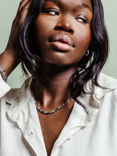 Portrait of a woman wearing a silver-toned chain necklace with geometric circular links, paired with a white textured blouse.