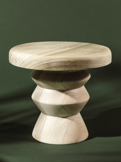 Minimalist pedestal stand crafted from light, unfinished natural wood with a smooth, rounded top and stacked, faceted base.