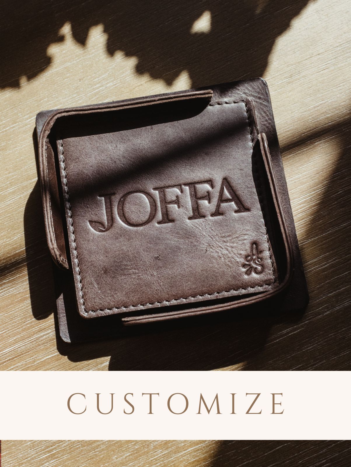 Square dark brown leather coaster set on wood table. Digital sticker to indicate product is customizable. 