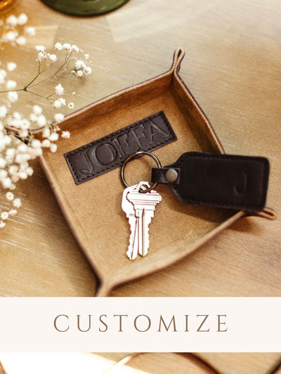 Small leather valet tray on wooden table with keys and leather key chain.Small leather valet tray on wooden table with keys and leather key chain. Digital sticker indicating the product is customizable. 