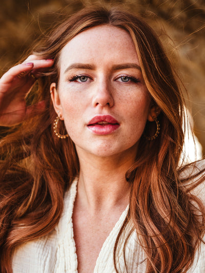 Portrait of female with red hair wearing gold brass disc hoop earrings