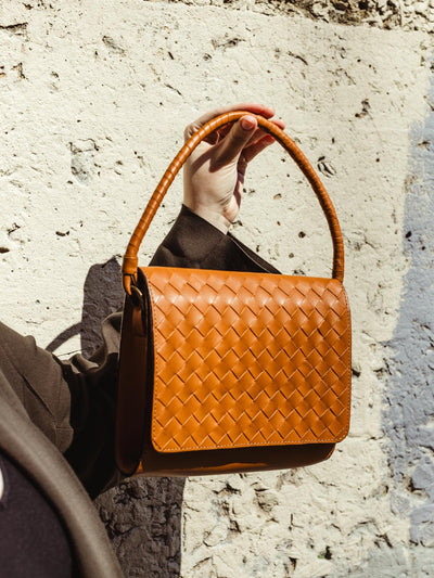 Model holding handmade leather bag on concrete textured background.