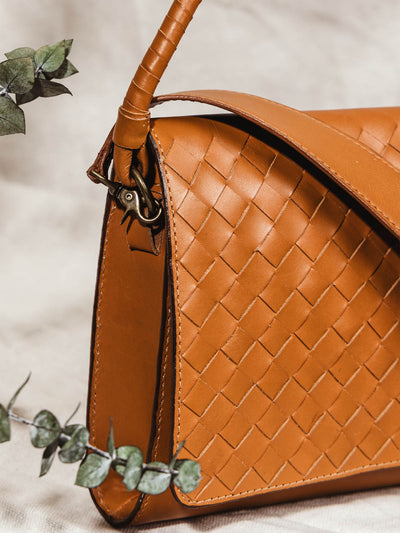Side view of handmade braided leather bag on cloth background with some minimal greenery.