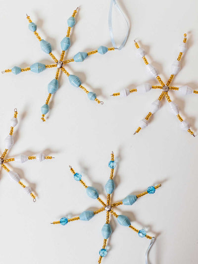 Light blue and white paper bead snowflake ornaments with gold bead accents, arranged on a white background for holiday décor.