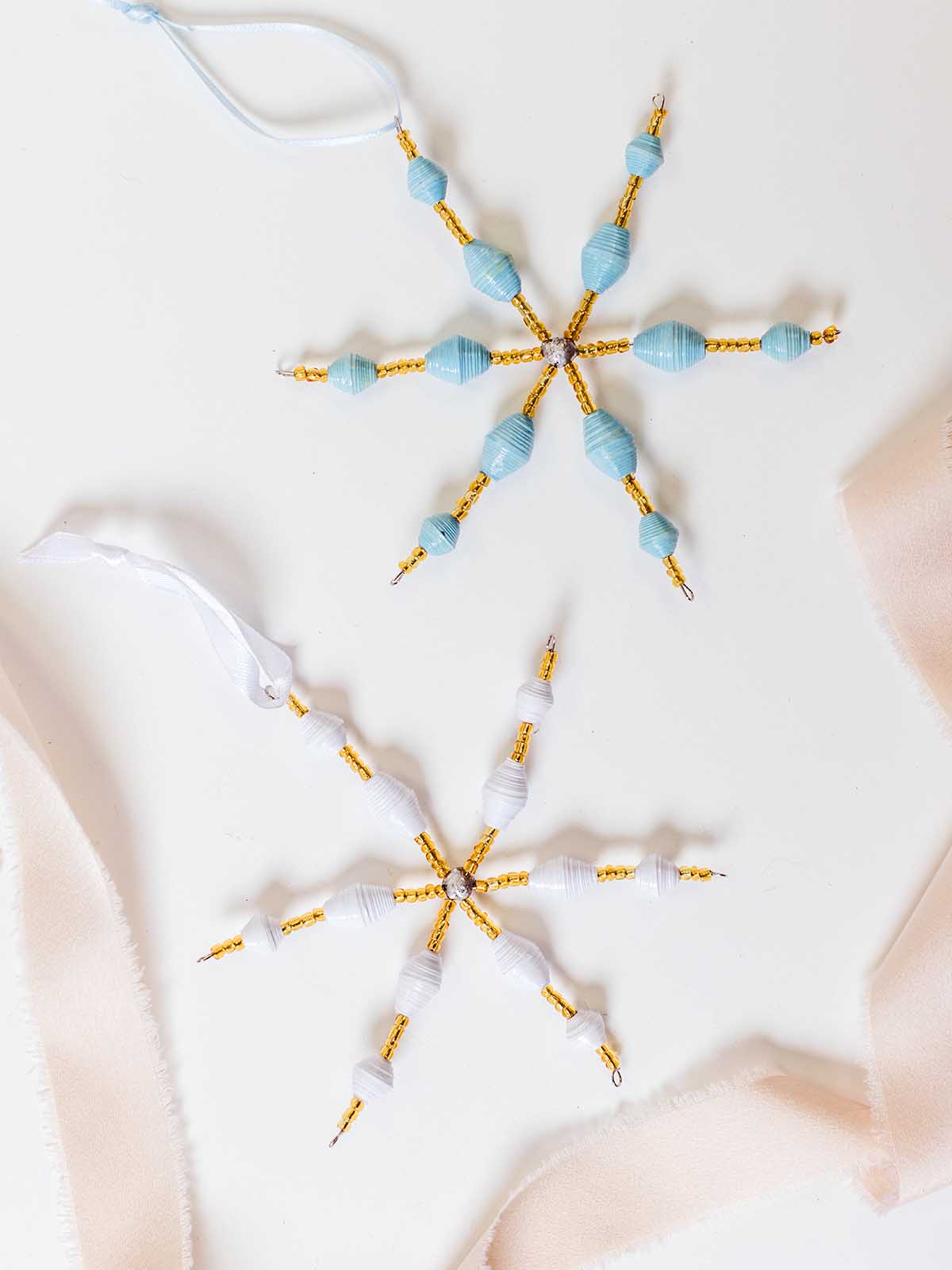 Set of blue and white handcrafted paper bead snowflake ornaments with gold accents, styled with soft neutral ribbon for gift-ready presentation.