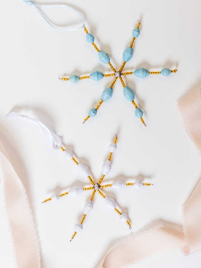 Set of blue and white handcrafted paper bead snowflake ornaments with gold accents, styled with soft neutral ribbon for gift-ready presentation.