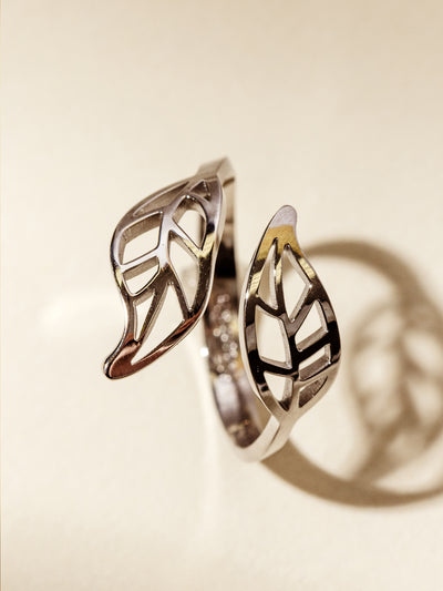 Detailed close-up of a silver wrap ring featuring two intricate leaf shapes, casting a soft shadow on a neutral surface.
