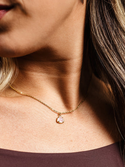 Detailed close-up of a gold necklace featuring a faceted, soft pink gemstone pendant in a gold prong setting. The delicate chain rests against the model’s collarbone, adding a subtle and refined touch.