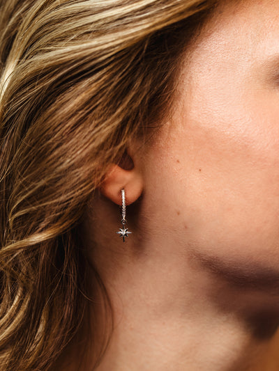 Close-up of a silver hoop earring with pavé stones and star charm worn by a woman with wavy blonde hair.