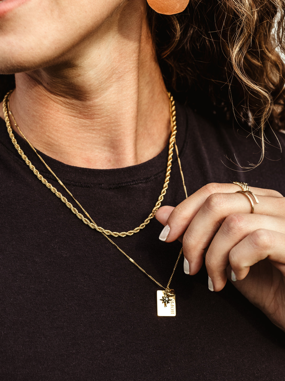 Closeup of gold hope charm on hope statement necklace on white female model. 