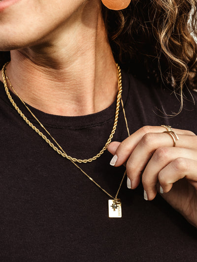 Closeup of gold hope charm on hope statement necklace on white female model. 
