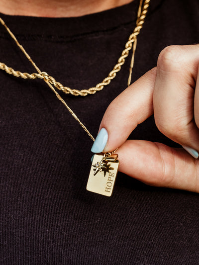 Closeup of gold hope charm on hope statement necklace. 