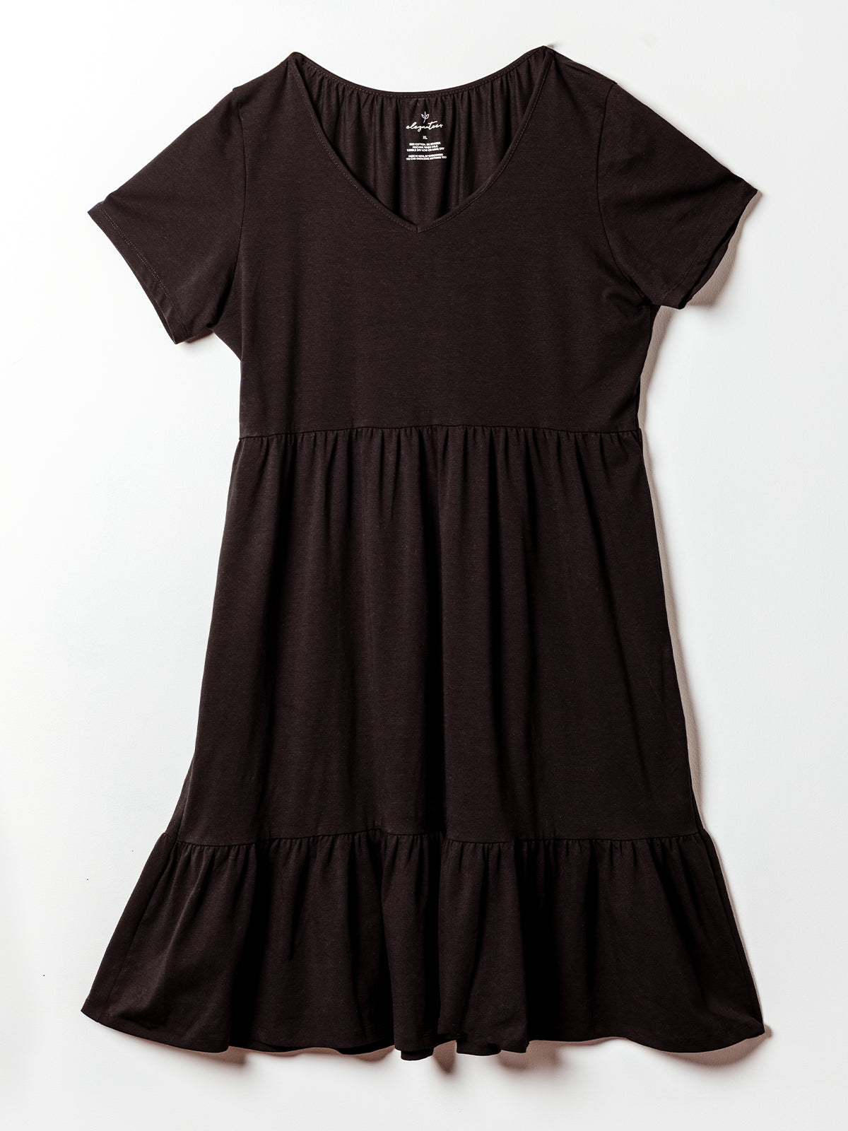 A black short-sleeve midi dress is laid flat against a white background. The dress features a V-neckline, empire waist, and tiered skirt with gentle gathers, creating a soft, flowy silhouette. Made from a stretchy knit fabric, it offers a comfortable and casual yet feminine style.